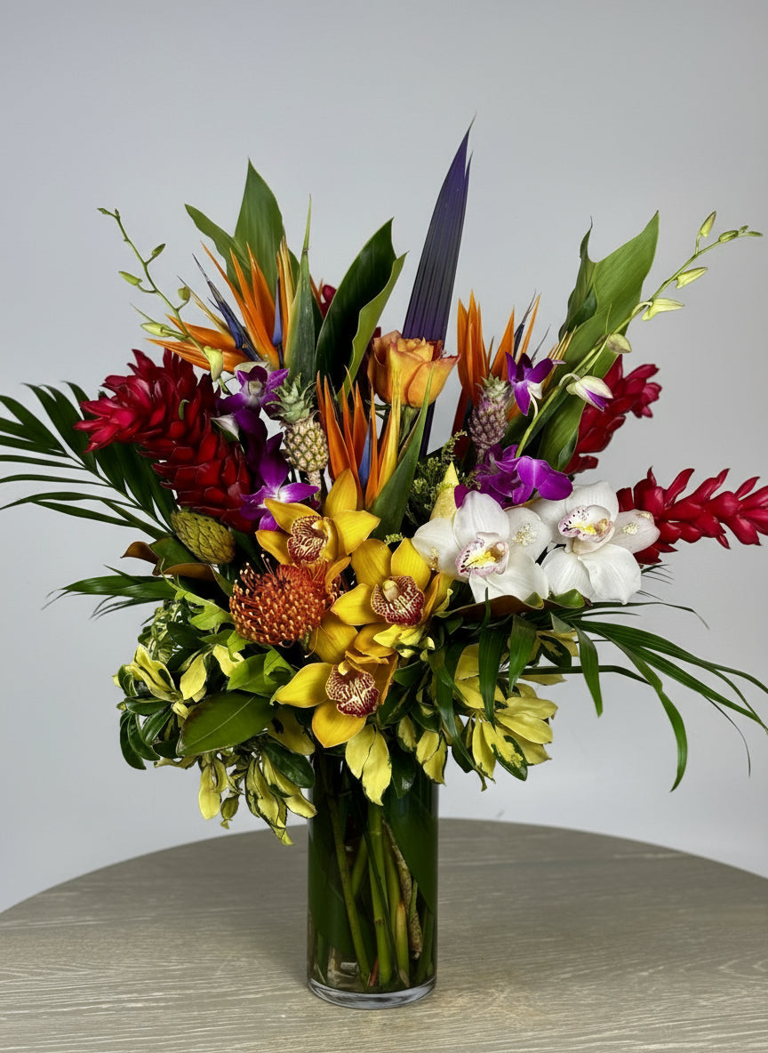 Colorful bouquet of tropical flowers in a clear vase on a wooden surface with a neutral background